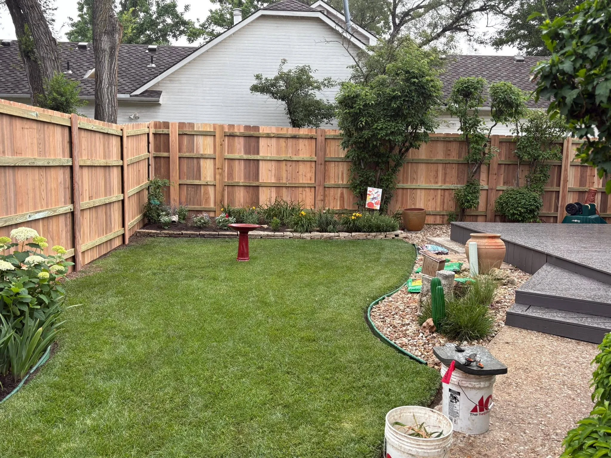 Wooden privacy fence with vertical boards and horizontal rails surrounding residential backyard with lawn and landscaping