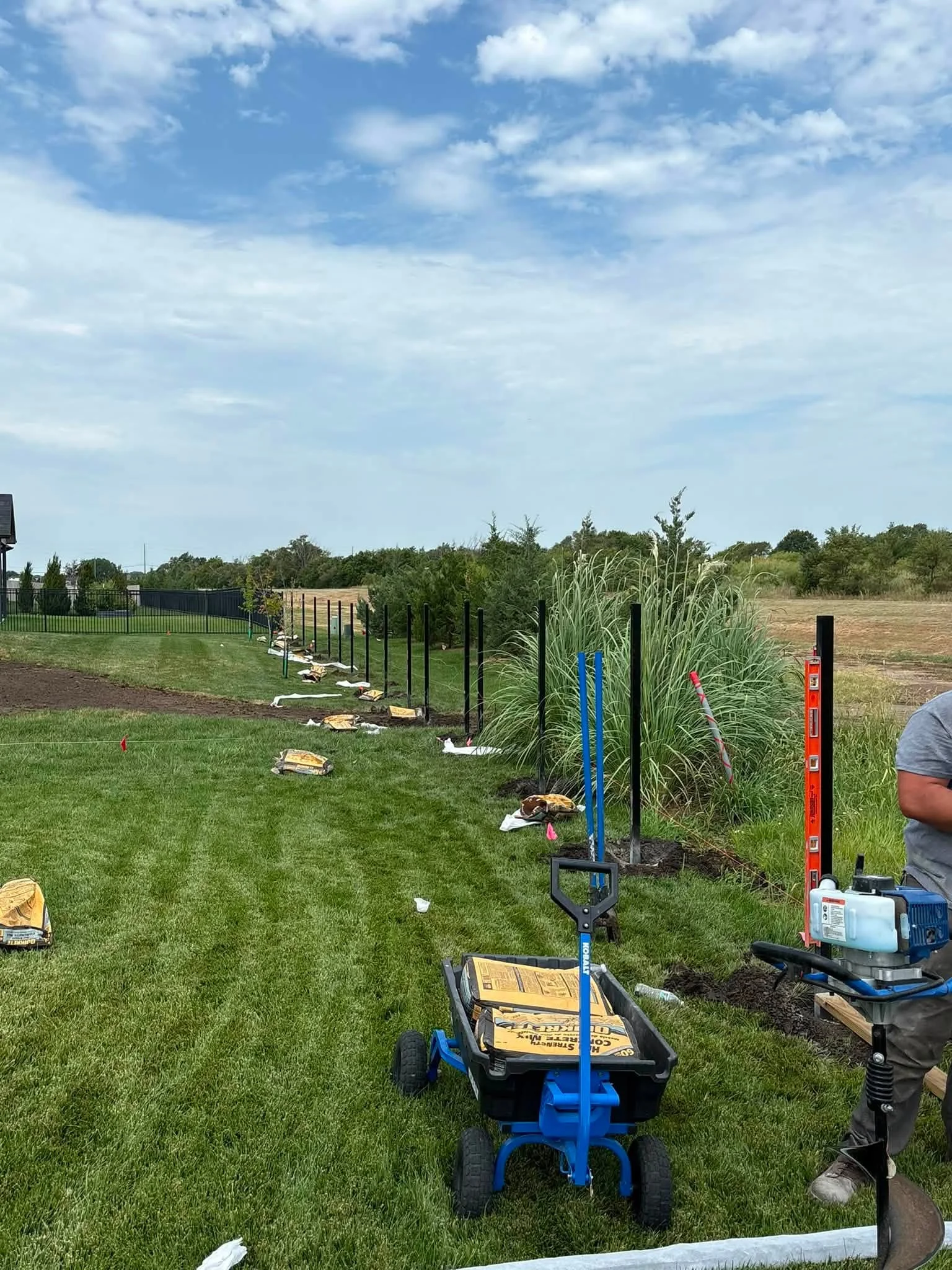 Black aluminum fence panels with ornamental grasses in landscape bed during installation