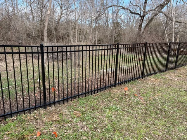 Black ornamental iron fence with vertical pickets and horizontal rails installed on residential property