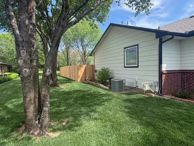 Wood privacy fence installed along residential yard with mature trees and green lawn