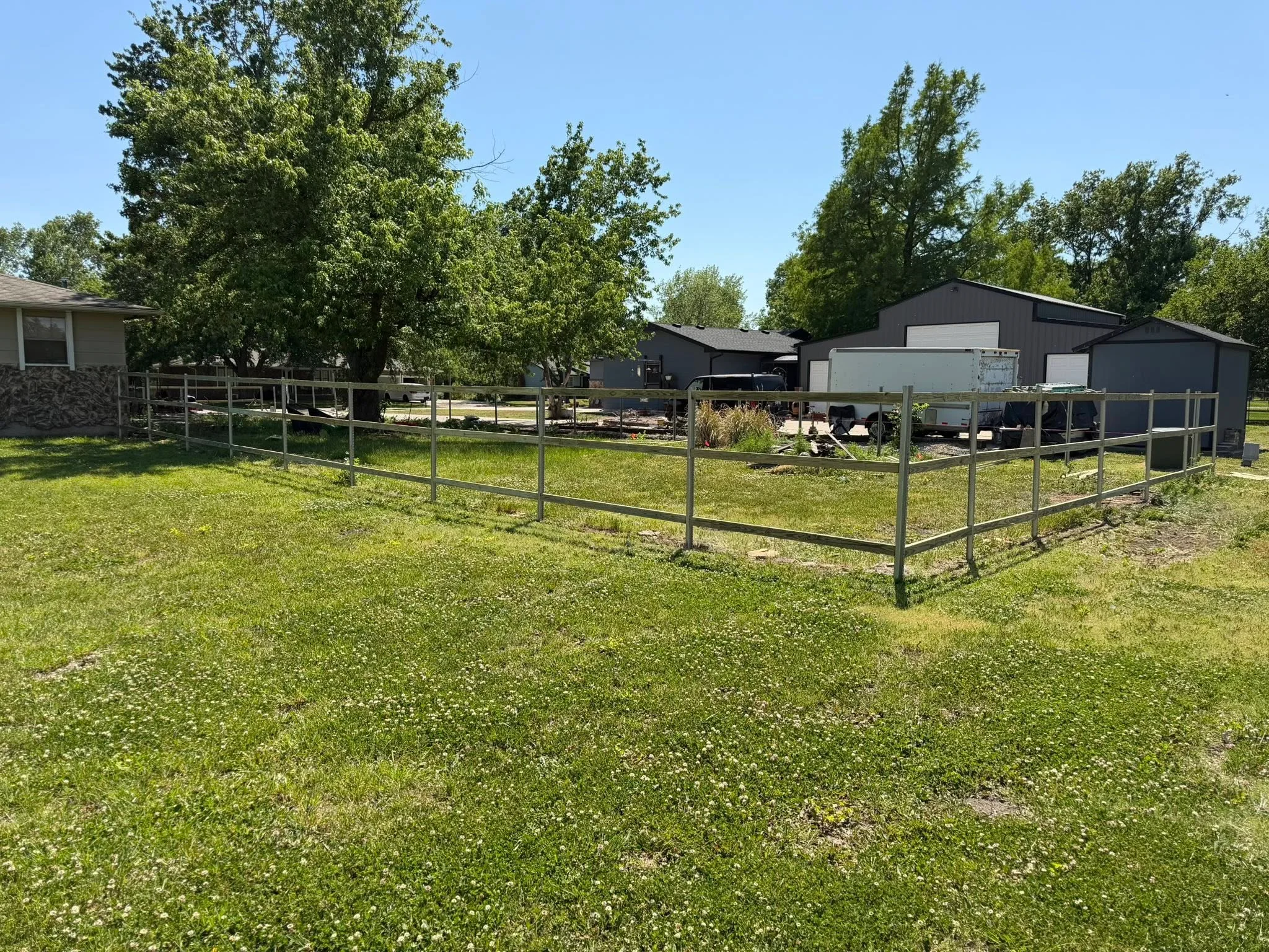 Steel pipe and rail fence with welded construction around pasture area with farm buildings