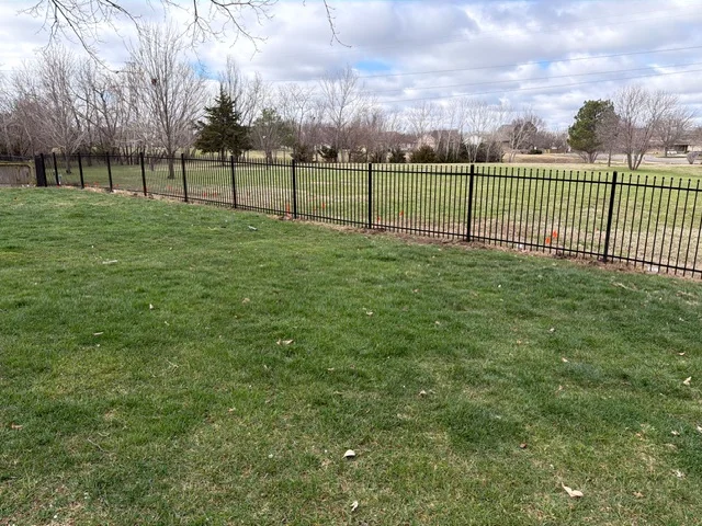 Black ornamental iron fence with vertical pickets installed along property line with mulch base