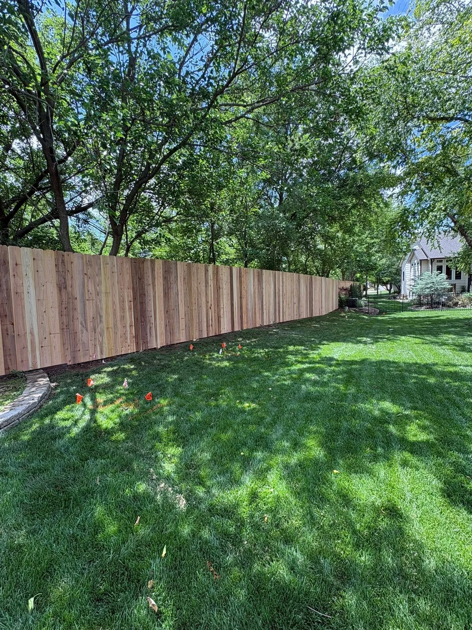 Vertical wood privacy fence with natural finish installed in residential backyard with mature trees