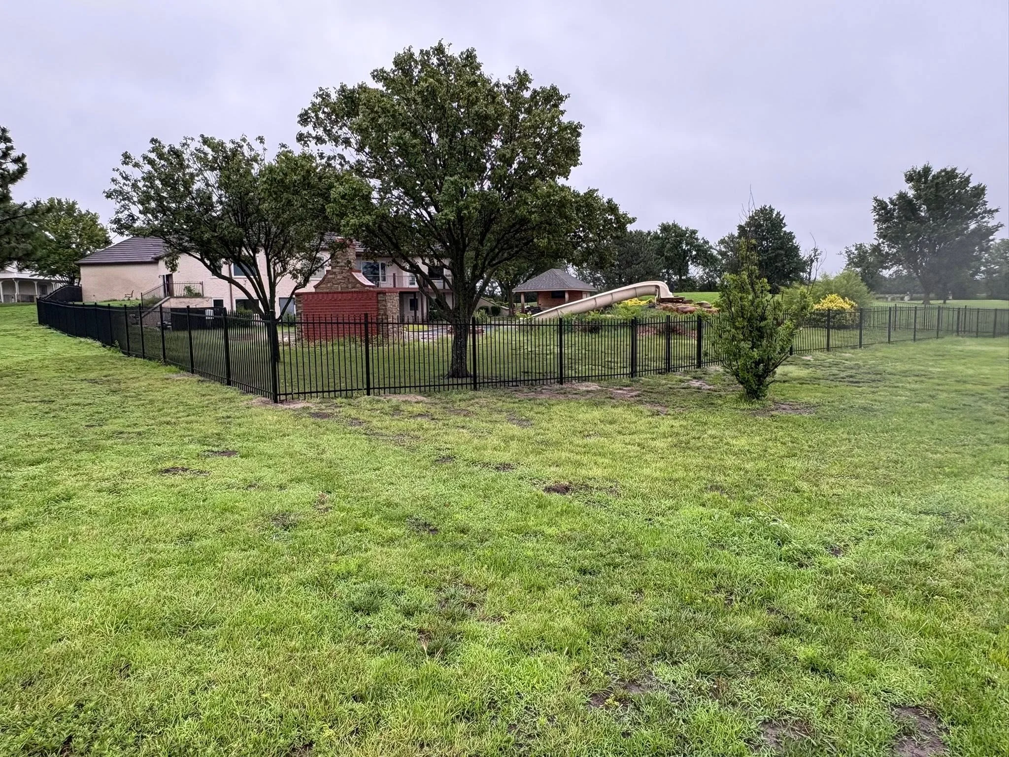 Black ornamental iron picket fence around residential property with mature trees
