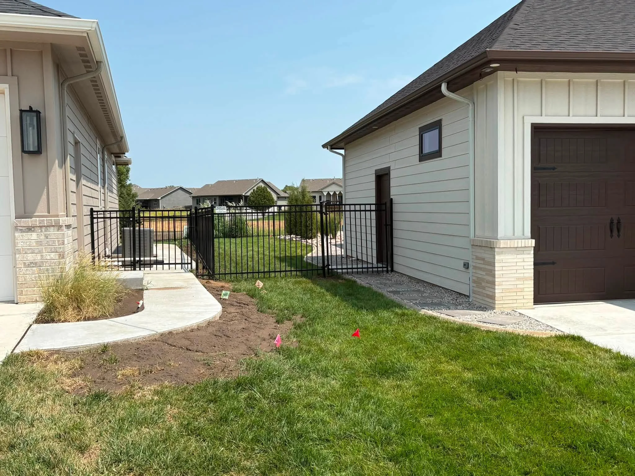 Black metal driveway gate with horizontal pickets installed between brick pillars at residential home entrance