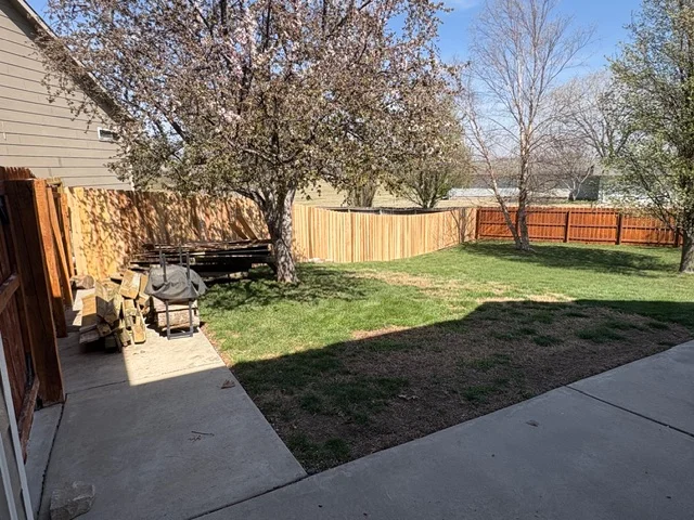 New vertical wood fence with stained finish installed around residential backyard perimeter