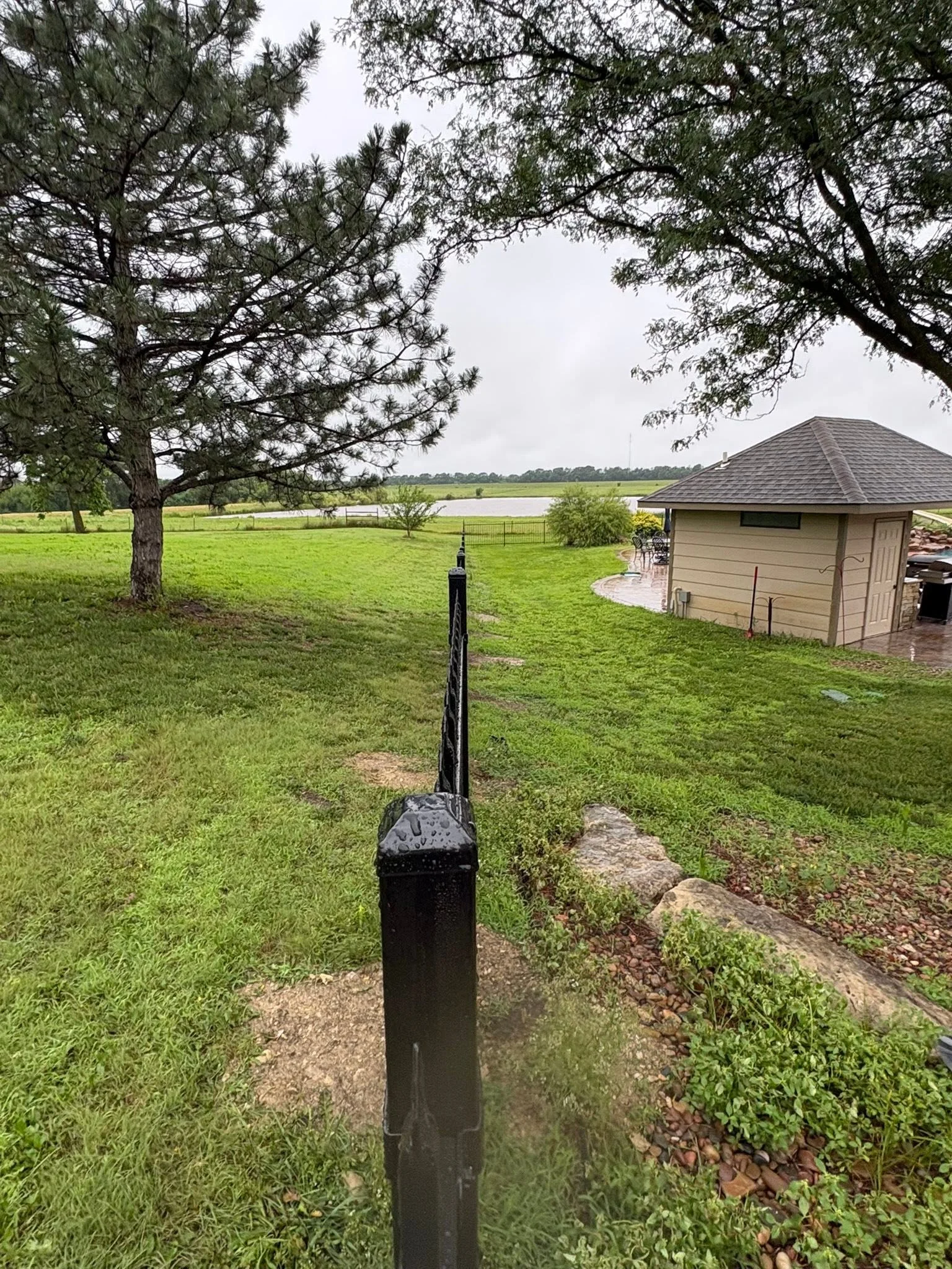 Black metal fence post with landscape edging on residential property with mature trees and waterfront view