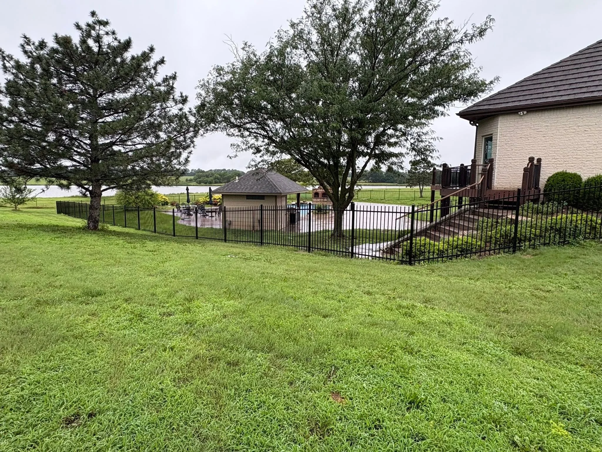 Black ornamental aluminum fence with picket design around waterfront residential property with mature trees
