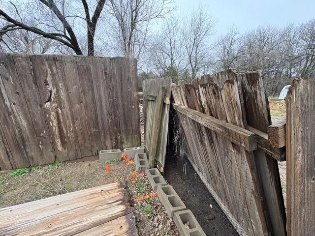 Dismantled wooden fence panels and posts with concrete blocks laid on ground for site preparation