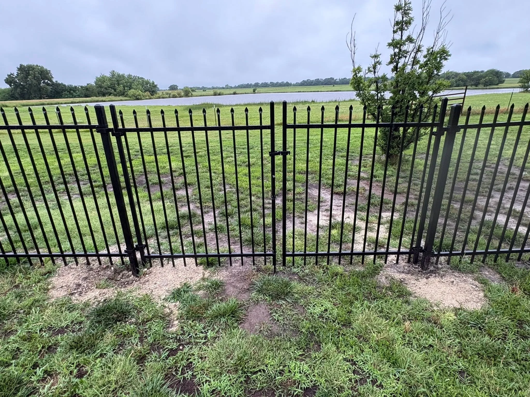 Black ornamental iron driveway gates with vertical pickets and finials, dual swing panels on gravel base